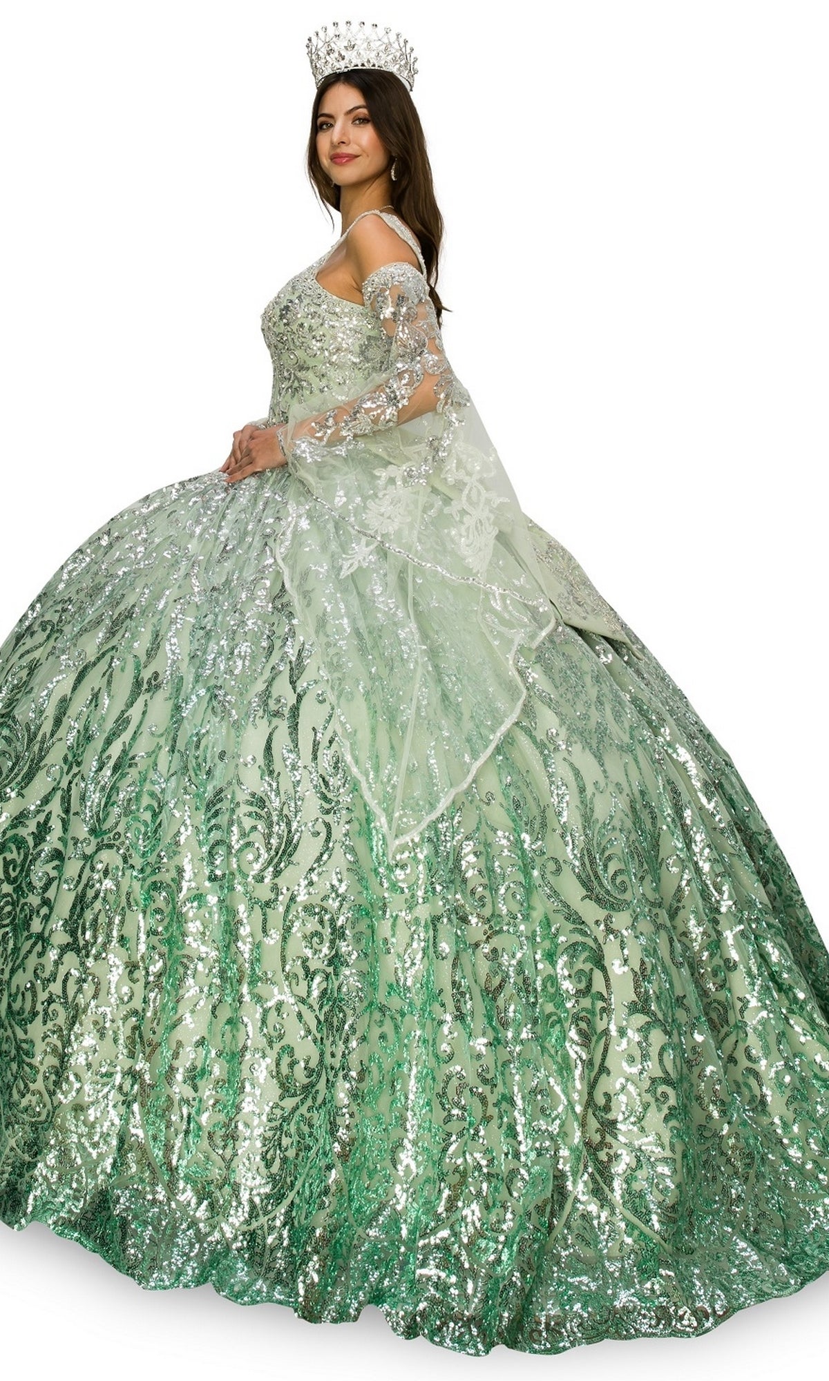 A woman models the Quinceanera Ball Gown 8080J, a sparkling green ombre dress with a full skirt and sheer shawl, finished with a jeweled crown as she stands slightly to the side.